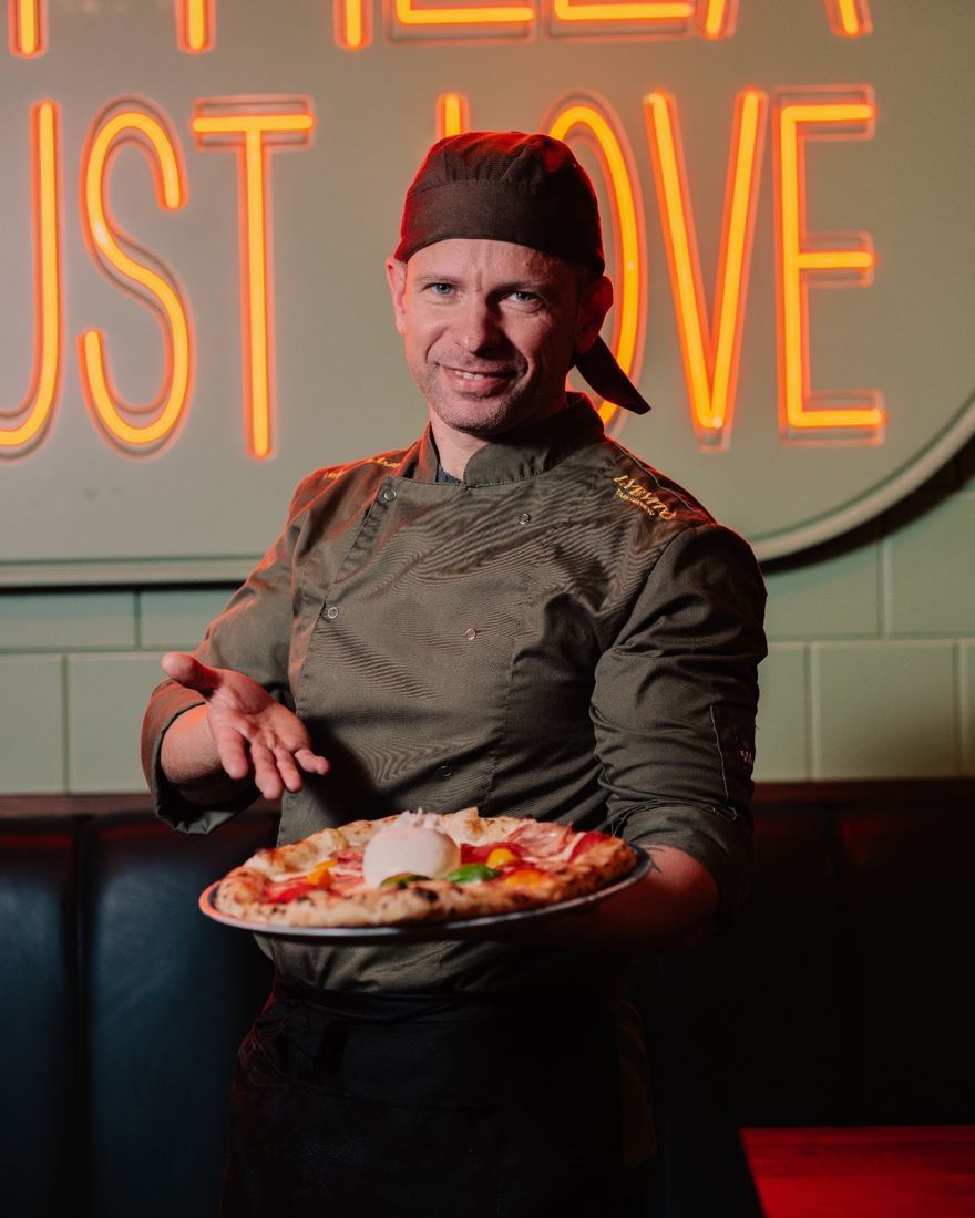 Vito Mantrone, titolare di Lyevitò, con una pizza in mano davanti all’insegna Eat Pizza Trust Love